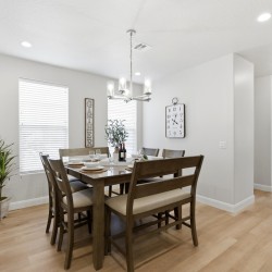 Dining room with a dark wood table set for six, a chandelier overhead, and a plant near the window.
