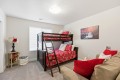 Cozy kids' bedroom with a dark wood bunk bed, red floral bedding, a ladder, and a beige sofa with red pillows; a waterfall wall art above.