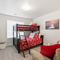 Cozy kids' bedroom with a dark wood bunk bed, red floral bedding, a ladder, and a beige sofa with red pillows; a waterfall wall art above.
