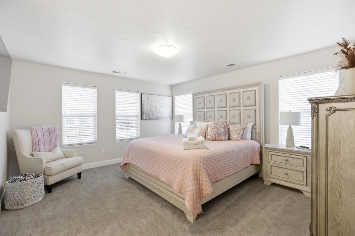 Bright neutral bedroom with a pink quilted bedspread, tufted headboard, and matching cream furniture.