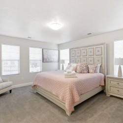Bright neutral bedroom with a pink quilted bedspread, tufted headboard, and matching cream furniture.