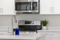 Modern kitchen scene with stainless steel microwave above a gas range, white cabinets, and a small potted plant on the counter.