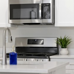 Modern kitchen scene with stainless steel microwave above a gas range, white cabinets, and a small potted plant on the counter.