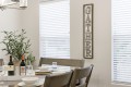Dining room table set for a meal with bowls, glasses, wine bottles, and a potted plant nearby; a rustic vertical GATHER sign on the wall.
