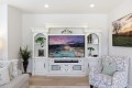 Elegant white entertainment center surrounding a flat-screen TV showing a poolside resort scene, with plants and decor on the shelves around it.