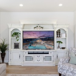 Elegant white entertainment center surrounding a flat-screen TV showing a poolside resort scene, with plants and decor on the shelves around it.