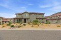 Two-story beige stucco house with a red tile roof and a desert rock yard in front of a suburban street
