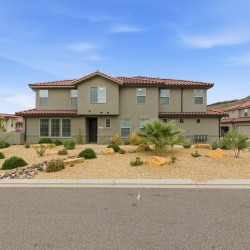 Two-story beige stucco house with a red tile roof and a desert rock yard in front of a suburban street
