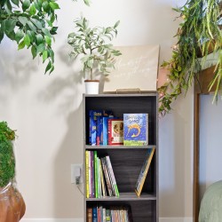 Gray wooden bookshelf framed by lush green plants, with a beige sign reading 'Mindset is everything' on top.
