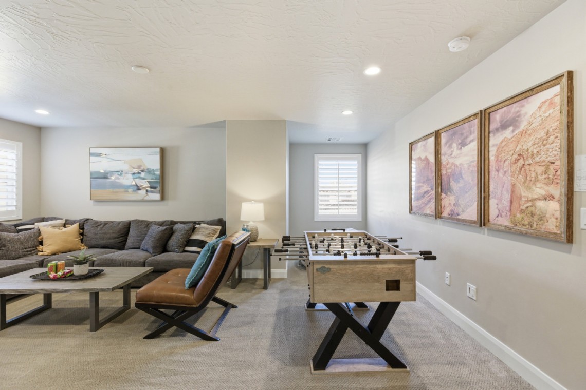 Basement recreation room with a foosball table, a gray sectional sofa, and a three-panel canyon wall art display.