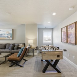 Basement recreation room with a foosball table, a gray sectional sofa, and a three-panel canyon wall art display.
