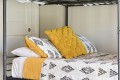 A neatly made bed with a white quilt featuring black geometric patterns and yellow accent pillows against a metal frame bed.