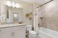Bright bathroom with a white vanity and sink, large mirror, three woven baskets on the wall, a toilet, and a tiled tub/shower with a white curtain.