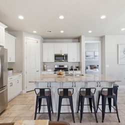 Open-concept kitchen with white cabinets, stainless steel fridge, granite island and six black bar stools at the counter.