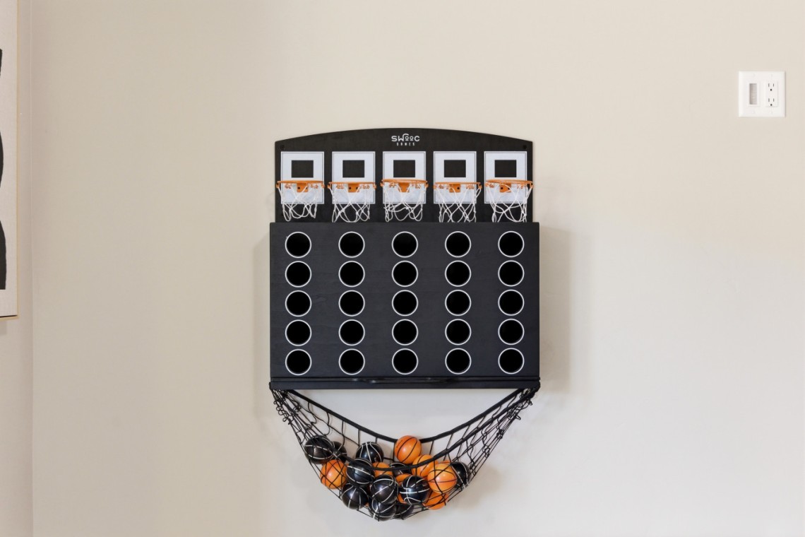 Black wall-mounted mini basketball arcade with multiple holes and a hanging net catching orange and black balls