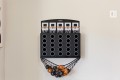 Black wall-mounted mini basketball arcade with multiple holes and a hanging net catching orange and black balls