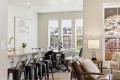 Open-concept kitchen and dining area with a marble island, black metal stools, and a wooden dining table set for dinner by bright windows.