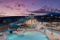 Community pool with a teal water slide, beige clubhouse, and lounge chairs at sunset with mountains in the distance.