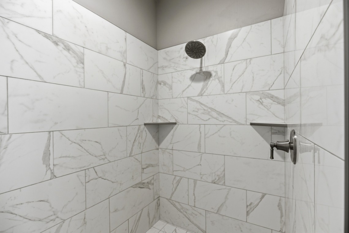 White marble-tiled shower with a round rainfall showerhead and a chrome control valve on the right wall
