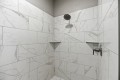 White marble-tiled shower with a round rainfall showerhead and a chrome control valve on the right wall