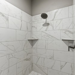 White marble-tiled shower with a round rainfall showerhead and a chrome control valve on the right wall