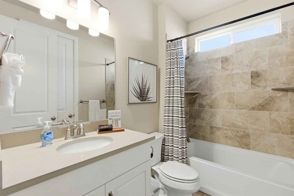 Modern bathroom with a white vanity, sink, large mirror, and soap dispenser beside a framed plant artwork
