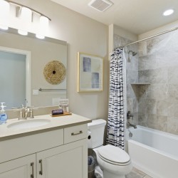 Bright bathroom with a white vanity, large mirror, and a striped shower curtain beside a tiled tub area.