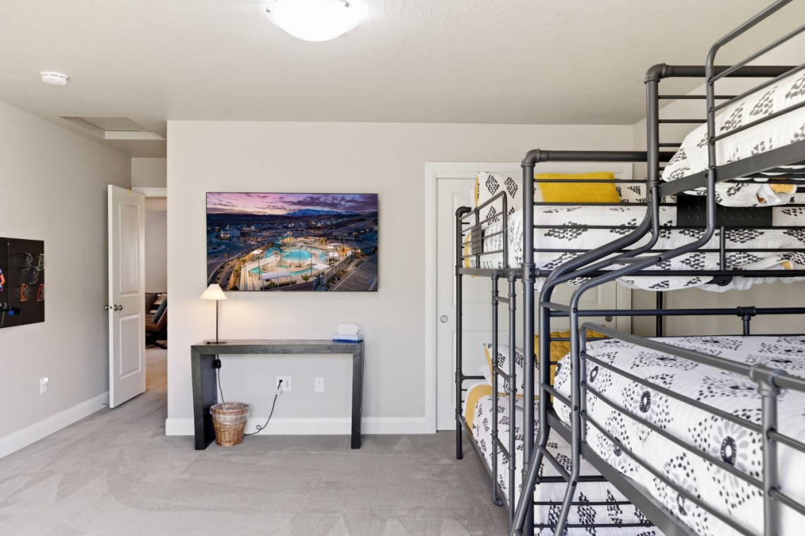 Dorm room with gray metal bunk beds on the right, a desk under a cityscape wall art, and an open doorway to a hallway.