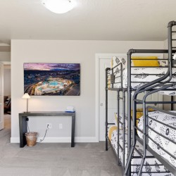 Dorm room with gray metal bunk beds on the right, a desk under a cityscape wall art, and an open doorway to a hallway.