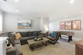 Spacious basement living room with a gray sectional sofa, a brown leather chair, and a dark wood coffee table; foosball table against the wall and framed canyon art above.