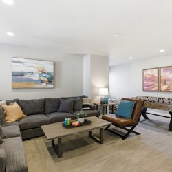 Spacious basement living room with a gray sectional sofa, a brown leather chair, and a dark wood coffee table; foosball table against the wall and framed canyon art above.