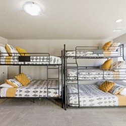 Two black metal bunk beds in a bright bedroom with gray-white patterned bedding and mustard pillows.