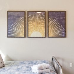 Three-panel sunburst artwork hung above a bed with blue pillows and folded towels on the blanket.