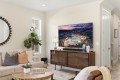 Modern living room with a wall-mounted flat-screen TV above a wooden media console, beige sofa with throw pillows, and a round-framed mirror on the wall.