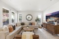 Bright living room with a beige L-shaped sofa, round wooden coffee table, and a large wall-mounted TV on a wooden console.