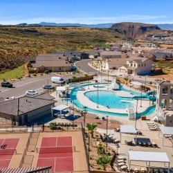 Aerial view of a desert resort-like community with a large central swimming pool, water slide, lounge chairs, and surrounding houses.