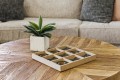 Wooden tic-tac-toe board on a round wooden table beside a potted plant.