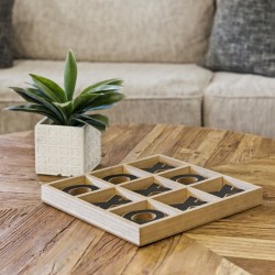 Wooden tic-tac-toe board on a round wooden table beside a potted plant.