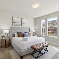 Bright modern bedroom with a king bed, gray upholstered headboard, two round wooden nightstands, and three large windows showing a rocky hillside outside.