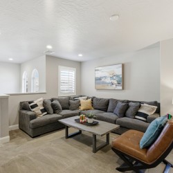 Cozy living room with a large gray sectional, rectangular coffee table, and a brown leather lounge chair. A lamp and framed art decorate the space.