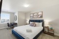 Hotel bedroom with a blue upholstered bed, white quilt, and two wood nightstands with lamps, plus three framed abstract landscape prints above the headboard.