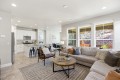 Open-concept living room and kitchen with a beige sectional, round wooden coffee table, and large windows overlooking a patio.