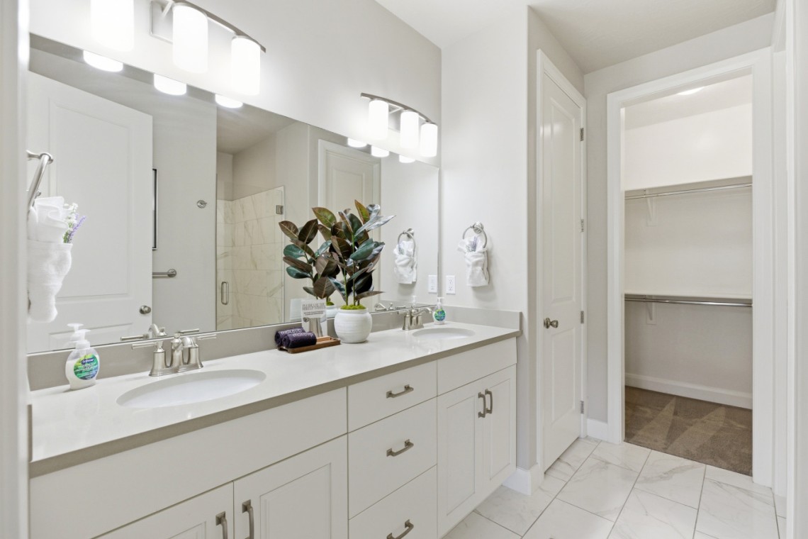 Bright bathroom with a white double vanity, two sinks, and a large mirror; open walk-in closet on the right.