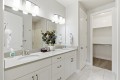 Bright bathroom with a white double vanity, two sinks, and a large mirror; open walk-in closet on the right.