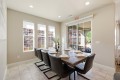 Dining room with a long wooden table set for six, black leather chairs, and a wine bottle centerpiece by a row of windows.