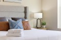 Bedroom with a padded gray headboard, decorative pillows, and a stack of white towels on a white comforter.