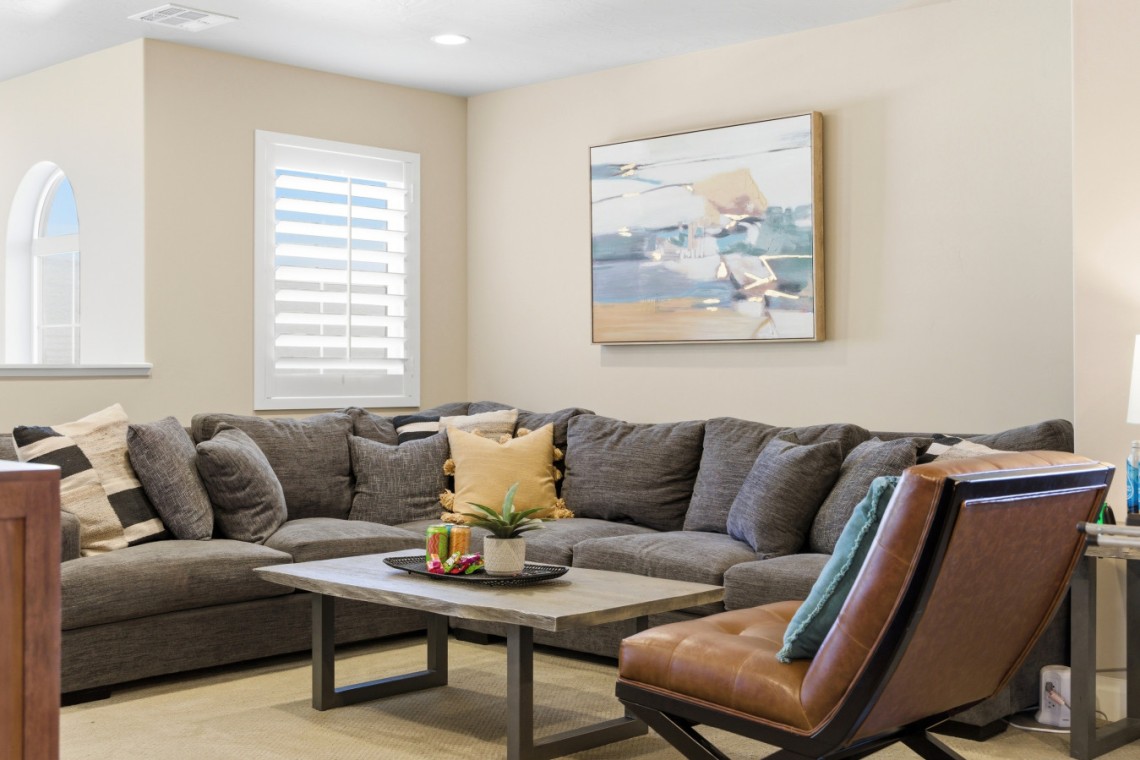 Cozy living room with a gray sectional sofa, a wood coffee table, potted plant, and abstract painting on beige walls.