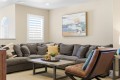 Cozy living room with a gray sectional sofa, a wood coffee table, potted plant, and abstract painting on beige walls.