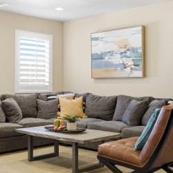 Cozy living room with a gray sectional sofa, a wood coffee table, potted plant, and abstract painting on beige walls.