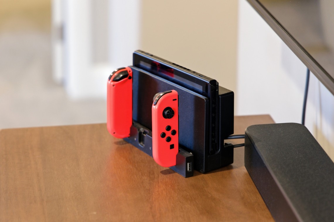 Nintendo Switch console in its dock with red Joy-Con controllers attached on a wooden table.